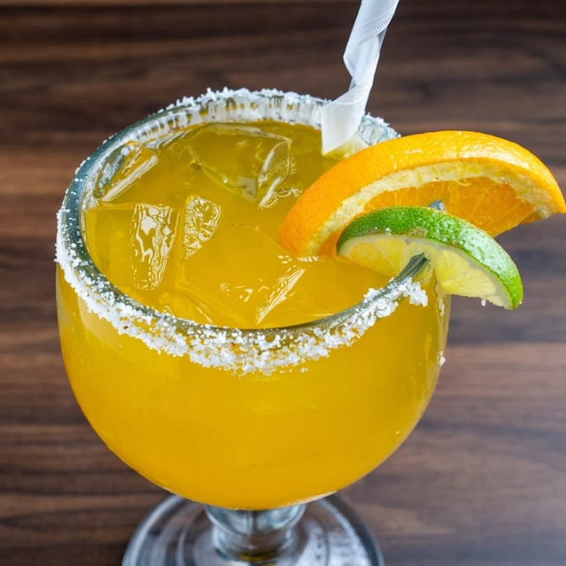 A vibrant yellow Habaneros margarita with ice, salt rim, orange slice, and lime wedge.