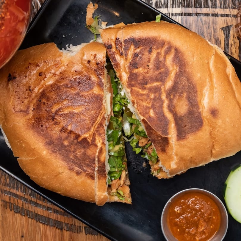 A large, toasted Mexican torta sandwich, cut in half, revealing chicken, lettuce, and sauce.