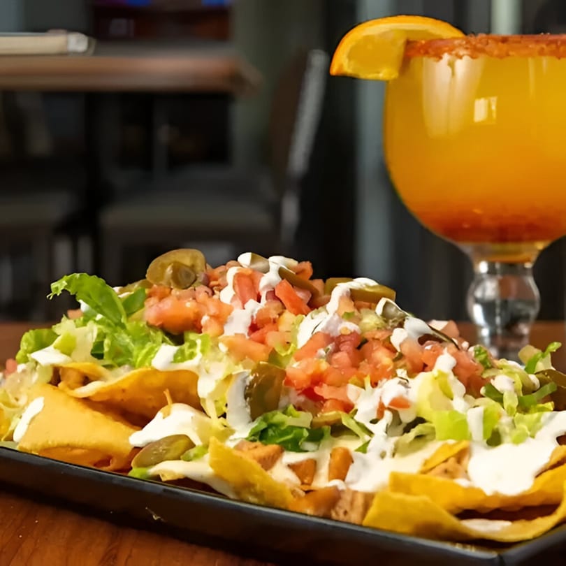 A plate of Habaneros Fresh Mexican Grill nachos with a margarita in the background.