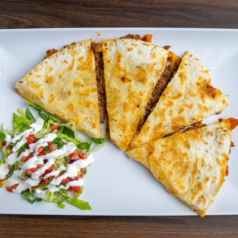 Four slices of beef quesadilla with a side of lettuce, pico de gallo, and sour cream.